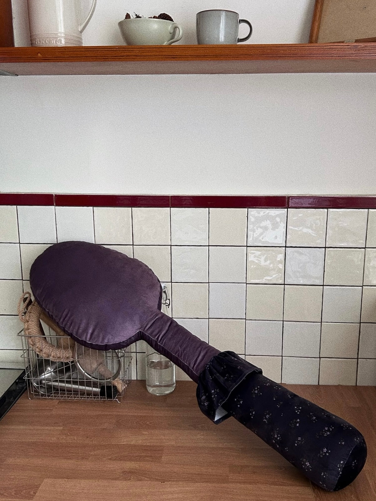 A purple spoon pillow rests diagonally, showing an oval head and a dark patterned handle with a gathered cuff.