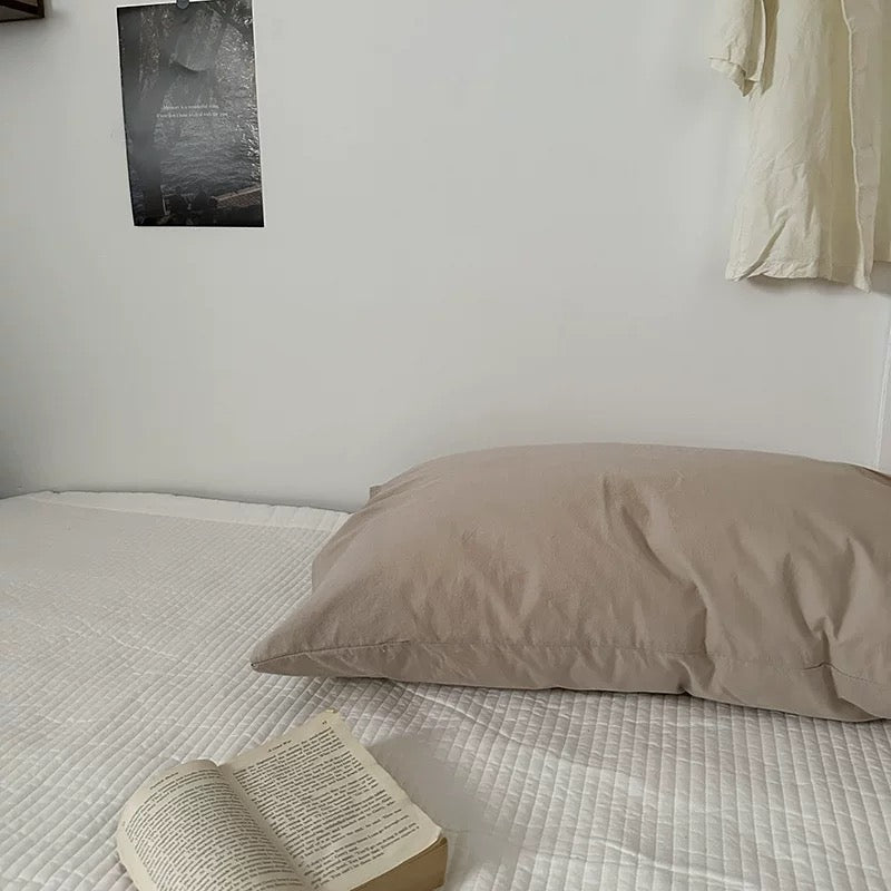 Beige pillow on a bed with an open book next to it, against a white wall.
