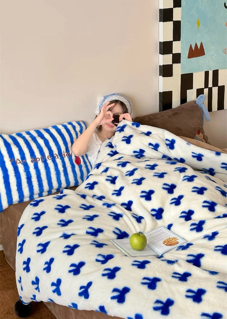 Person lying on a bed with a blue and white patterned blanket, surrounded by pillows and a colorful wall art piece.