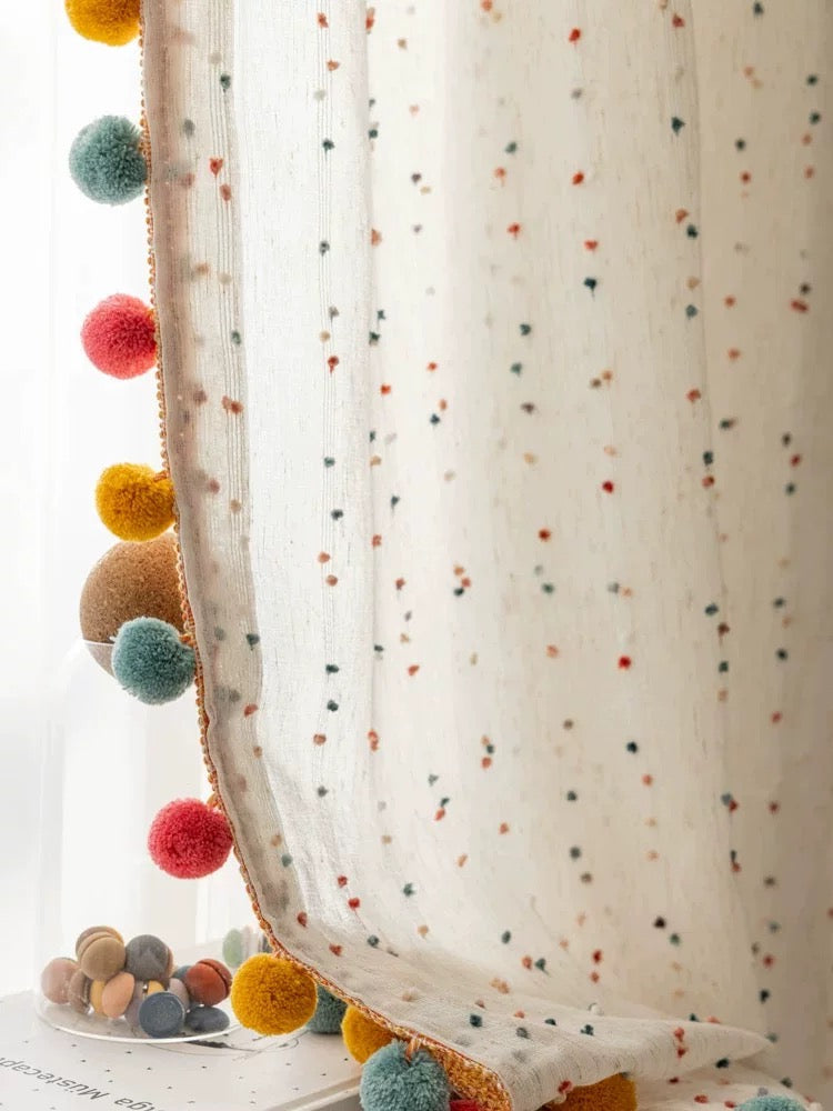 Decorative garland with colorful pom-poms held against a polka dot curtain.