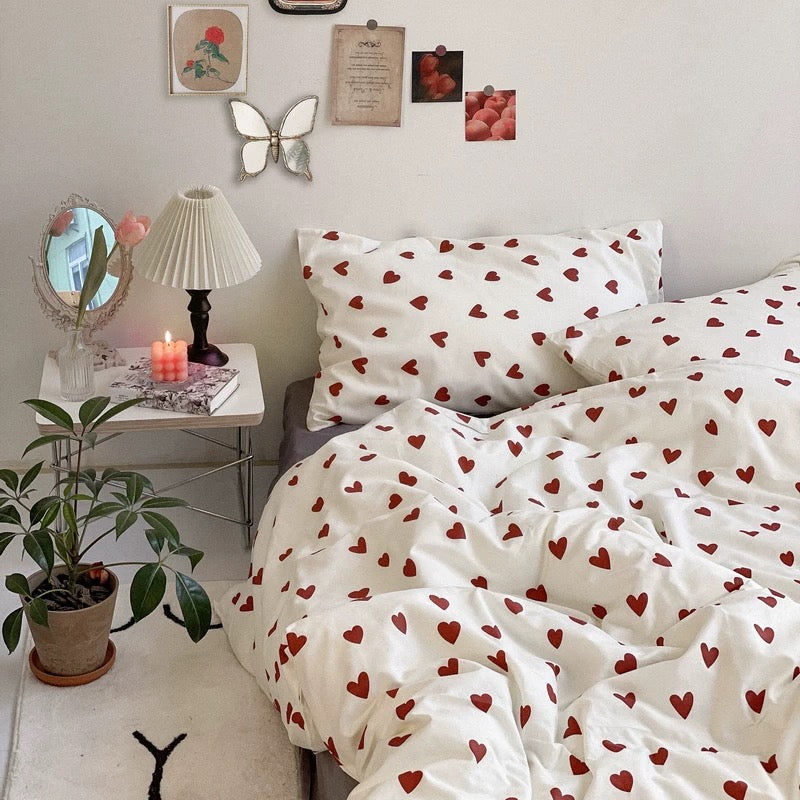 Red heart duvet cover on a styled bed with lamp, mirror, flowers and wall collage