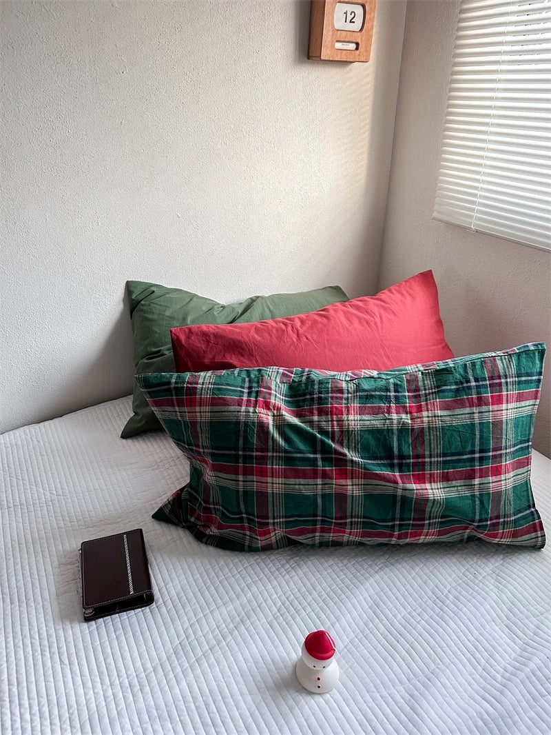 A red pillowcase and a green pillowcase sit behind a green tartan pillowcase with red and cream lines.