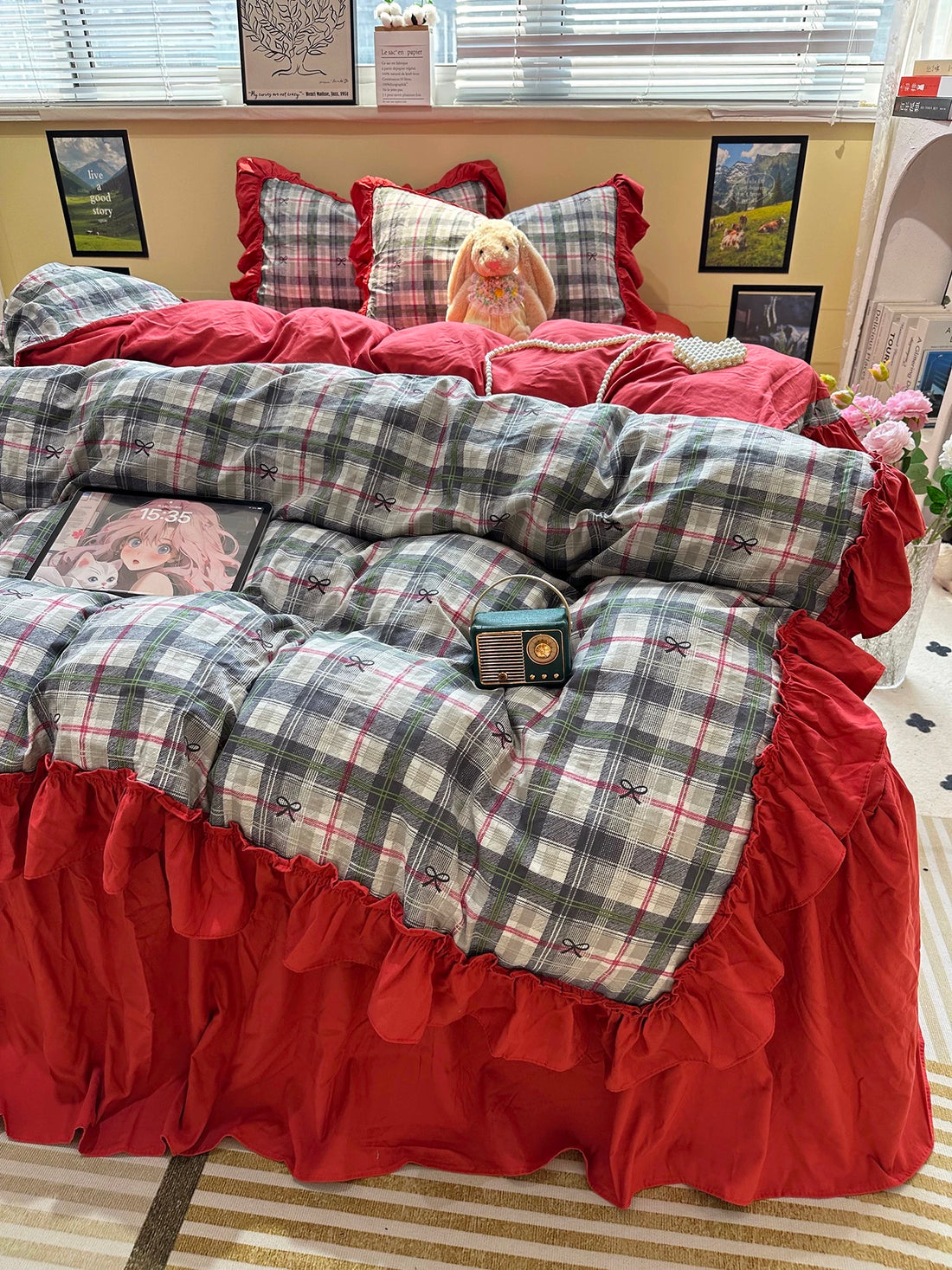 Bed with red and plaid bedding, teddy bear, and pink flowers.