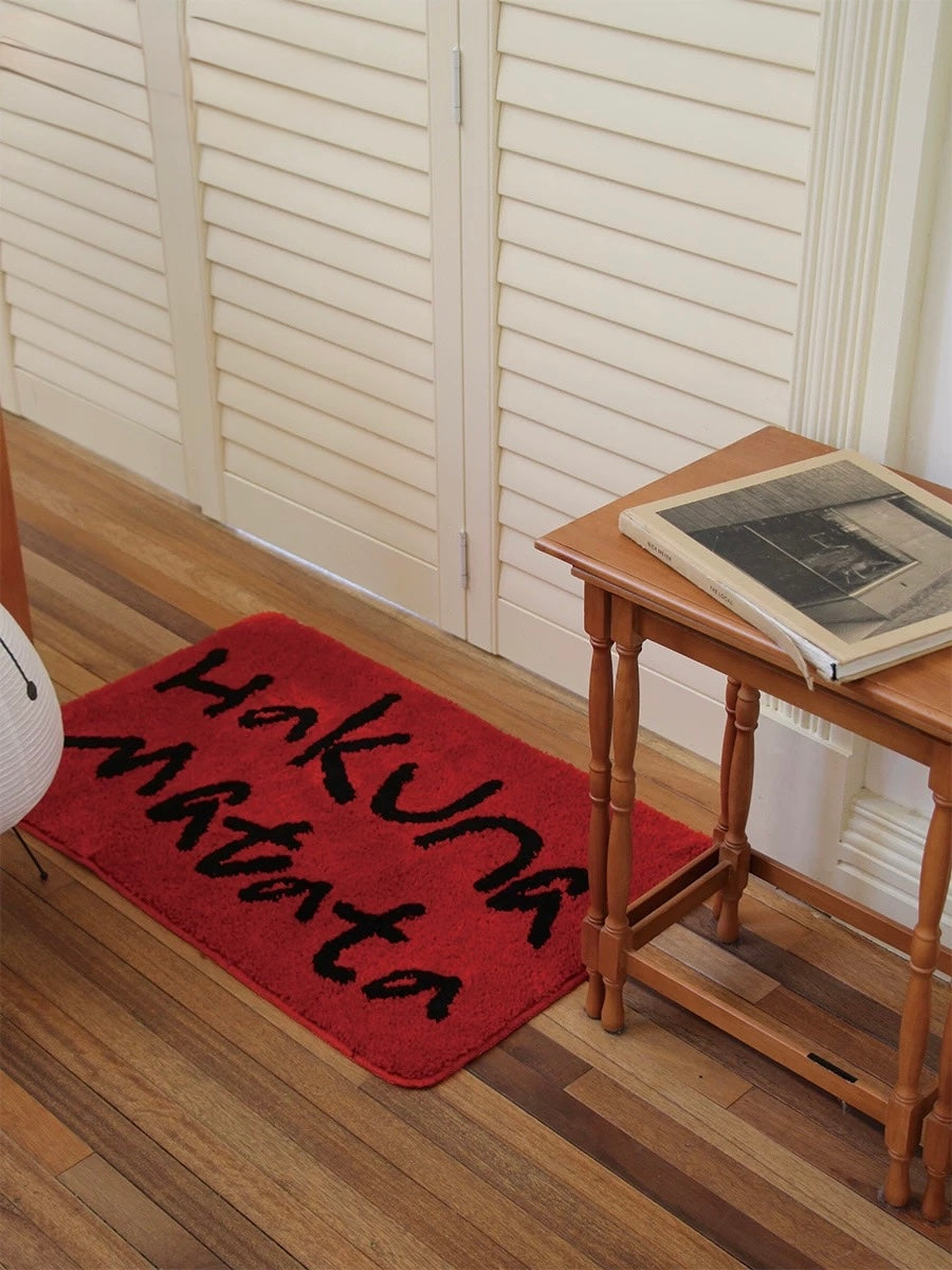 A red slogan floor mat lies in front of white folding doors beside a small stool on the floor.