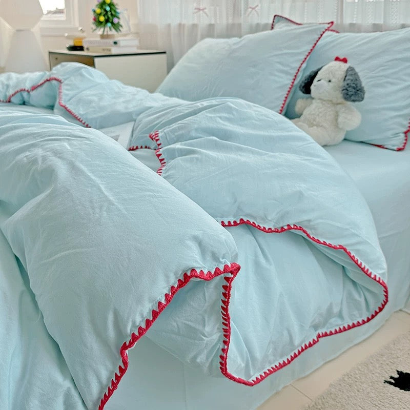 Light blue comforter with red trim on a bed in a bedroom setting.