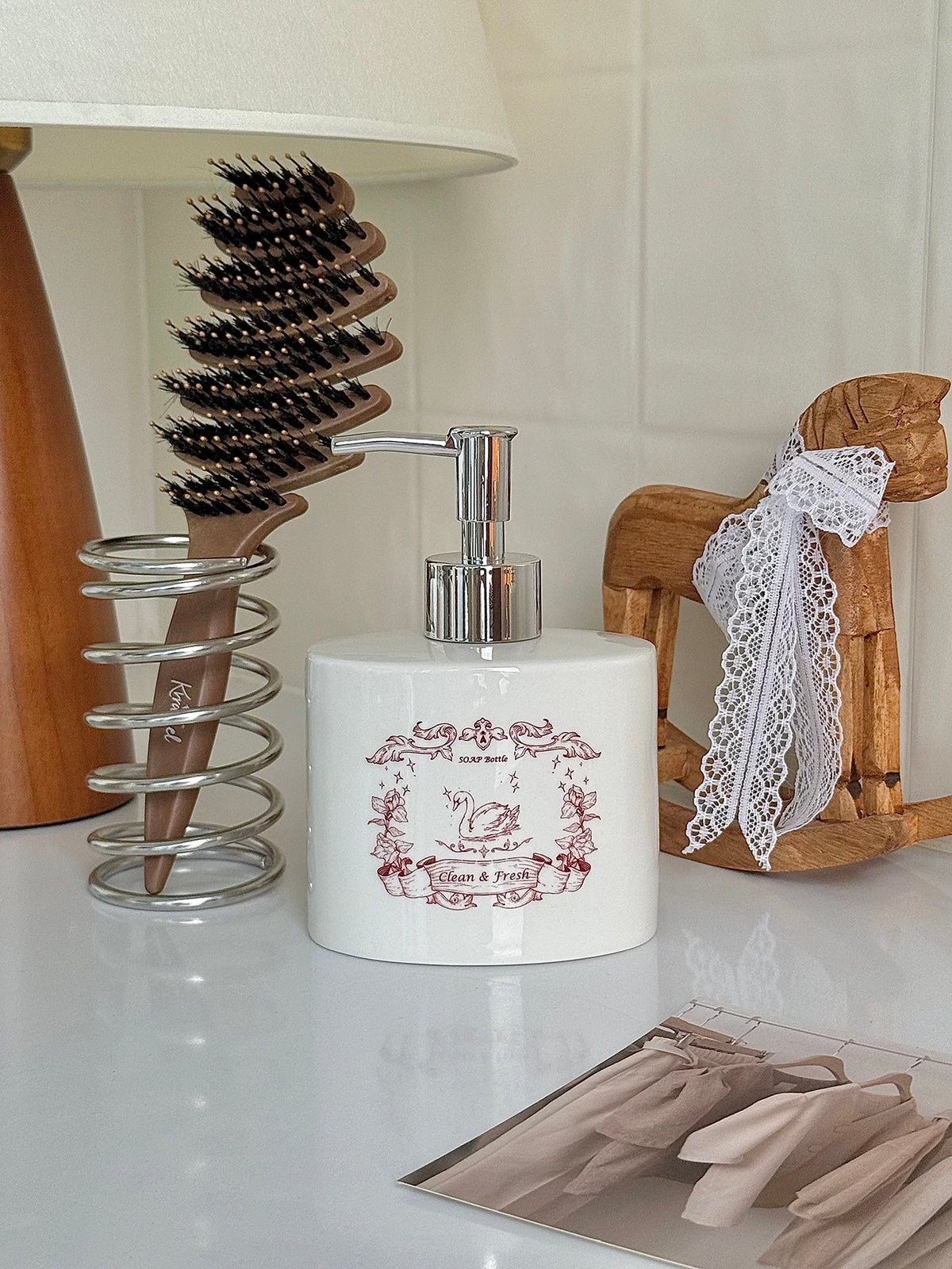 A red swan soap dispenser stands beside a hairbrush, with the illustrated front facing forward.