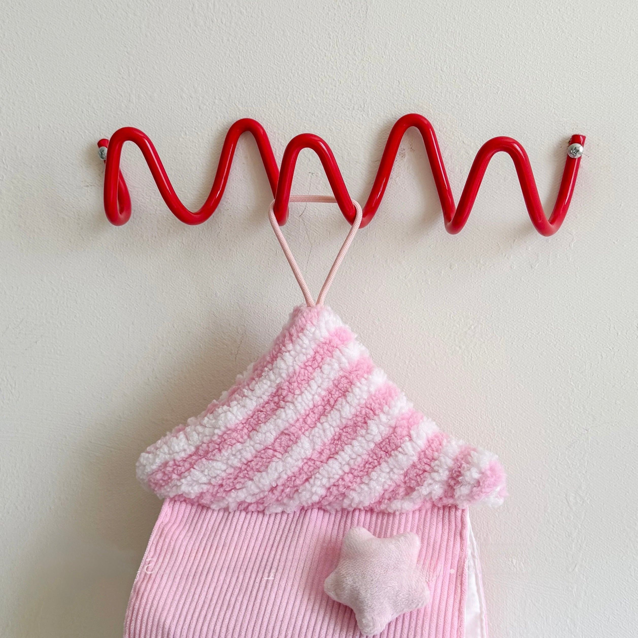Red wavy hook with pink and white striped fabric and star-shaped object on a light background