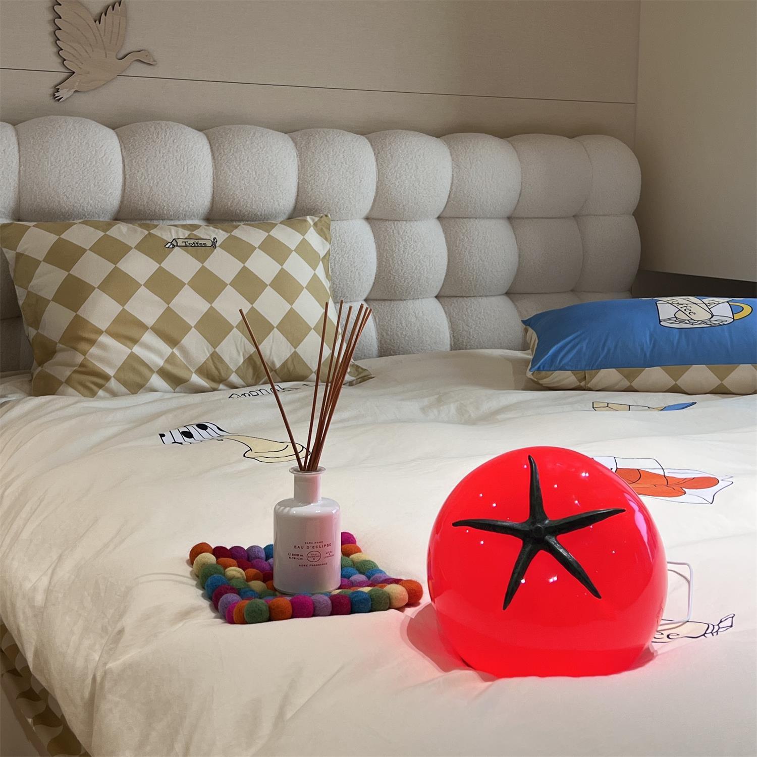 Decorative items on a bed including a diffuser, colorful coaster, and red star-shaped object.