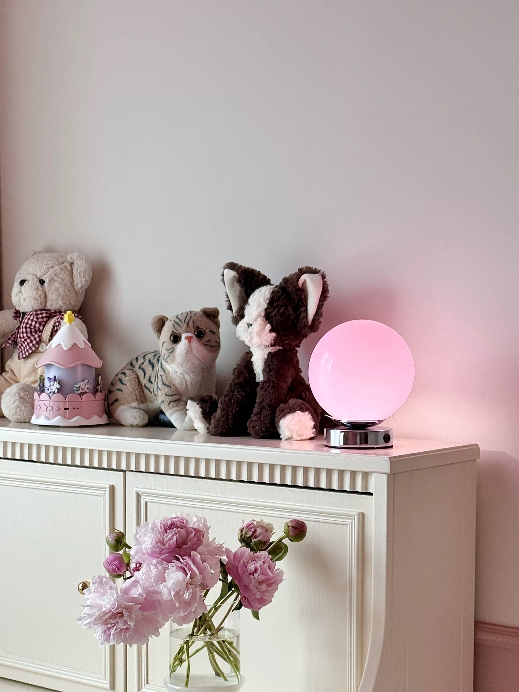 Decorative setup with plush toys and a glowing pink sphere on a white surface.