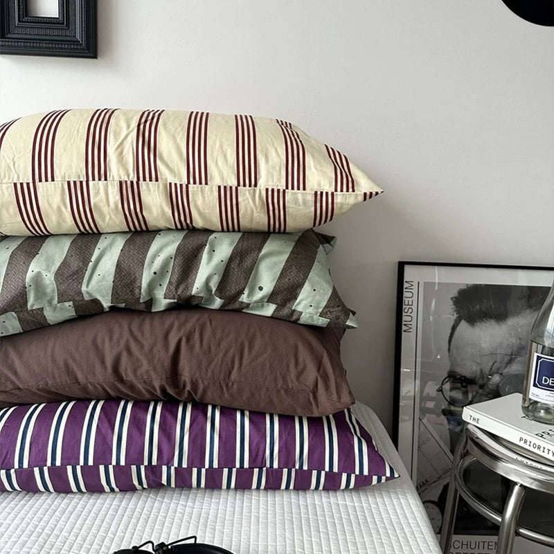 Stack of striped pillows on a bed with a framed picture and bottle in the background.