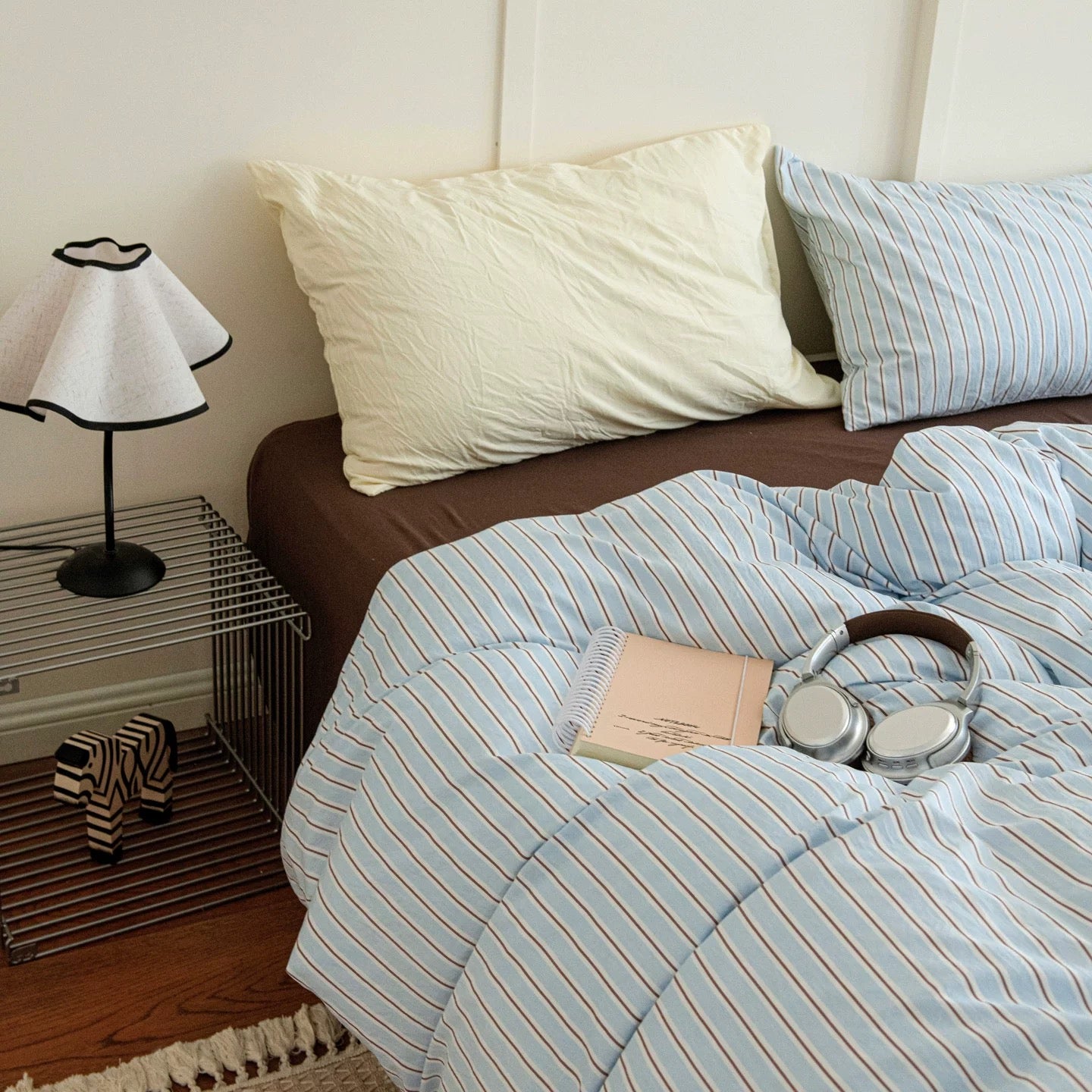Bed with striped bedding, pillows, and a lamp on a nightstand in a bedroom.
