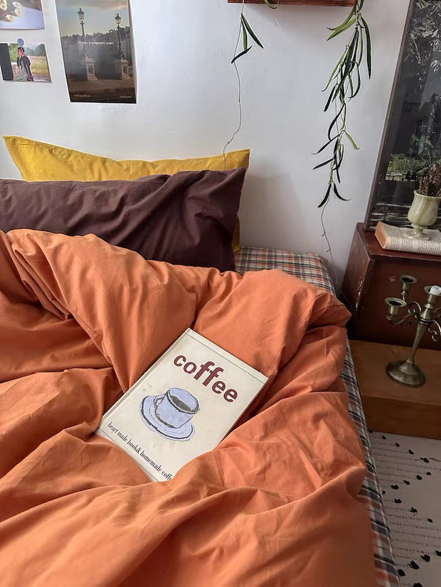Book titled 'coffee' under orange bedding on a bed with pillows and a plant in the background.