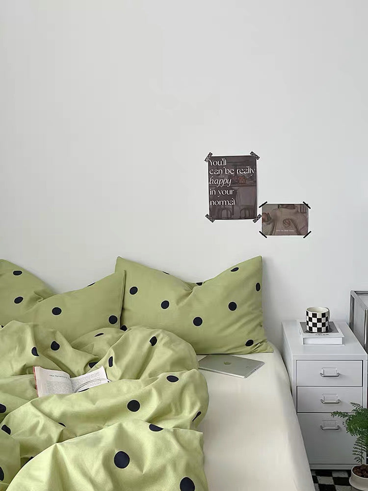 Bedroom with green polka dot bedding and a nightstand with books and a plant.