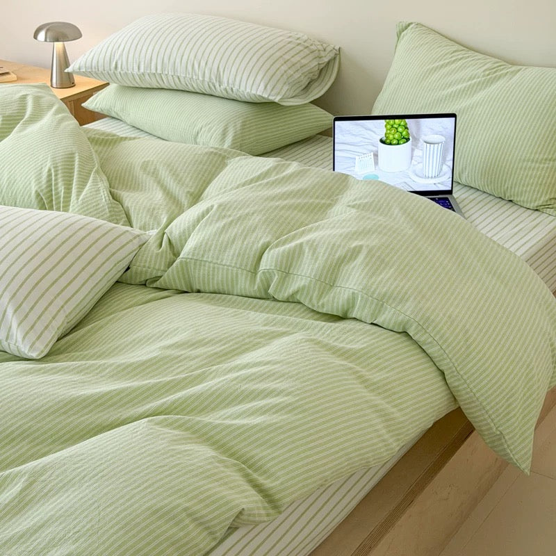 Light green and white striped bedding set on a bed, including a duvet cover, pillows, and a matching sheet, styled in a bedroom setting with a laptop on the bed.