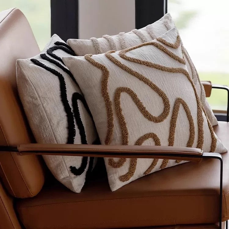 Decorative pillows with abstract patterns on a brown leather chair.