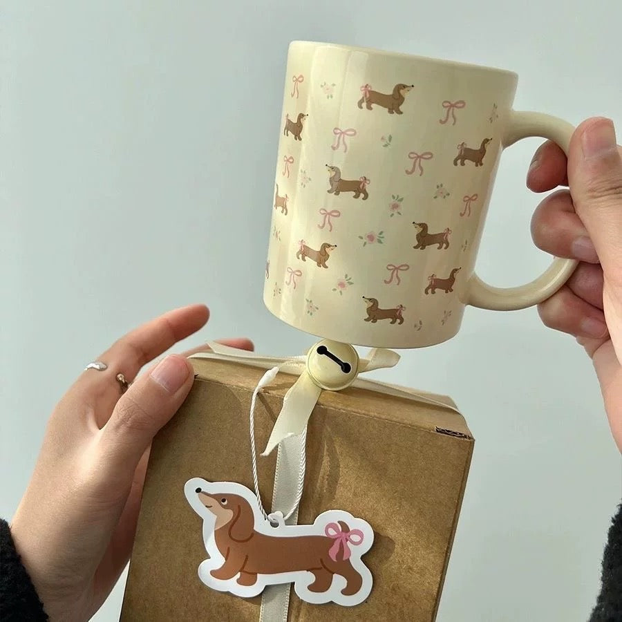 Mug with dachshund pattern held above a gift box with a decorative tag.