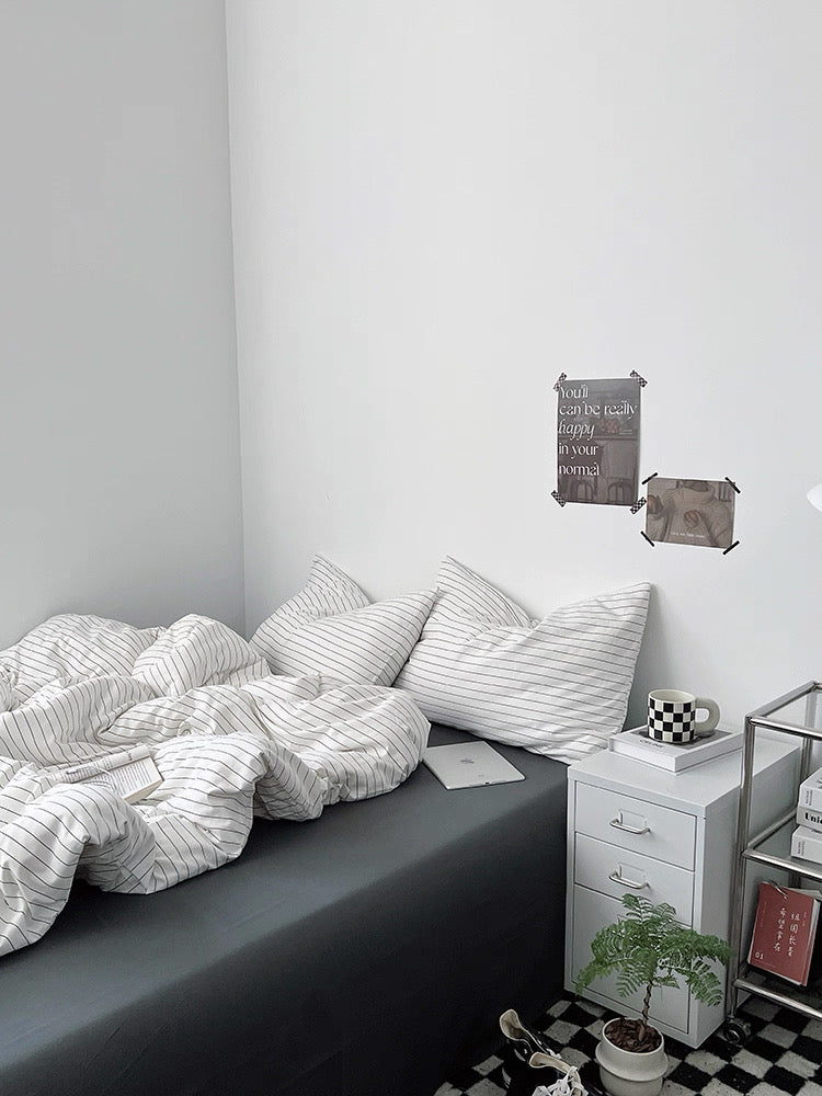 Bedroom with a bed featuring striped bedding and pillows, a nightstand with a plant and books, and decorative items on the wall.