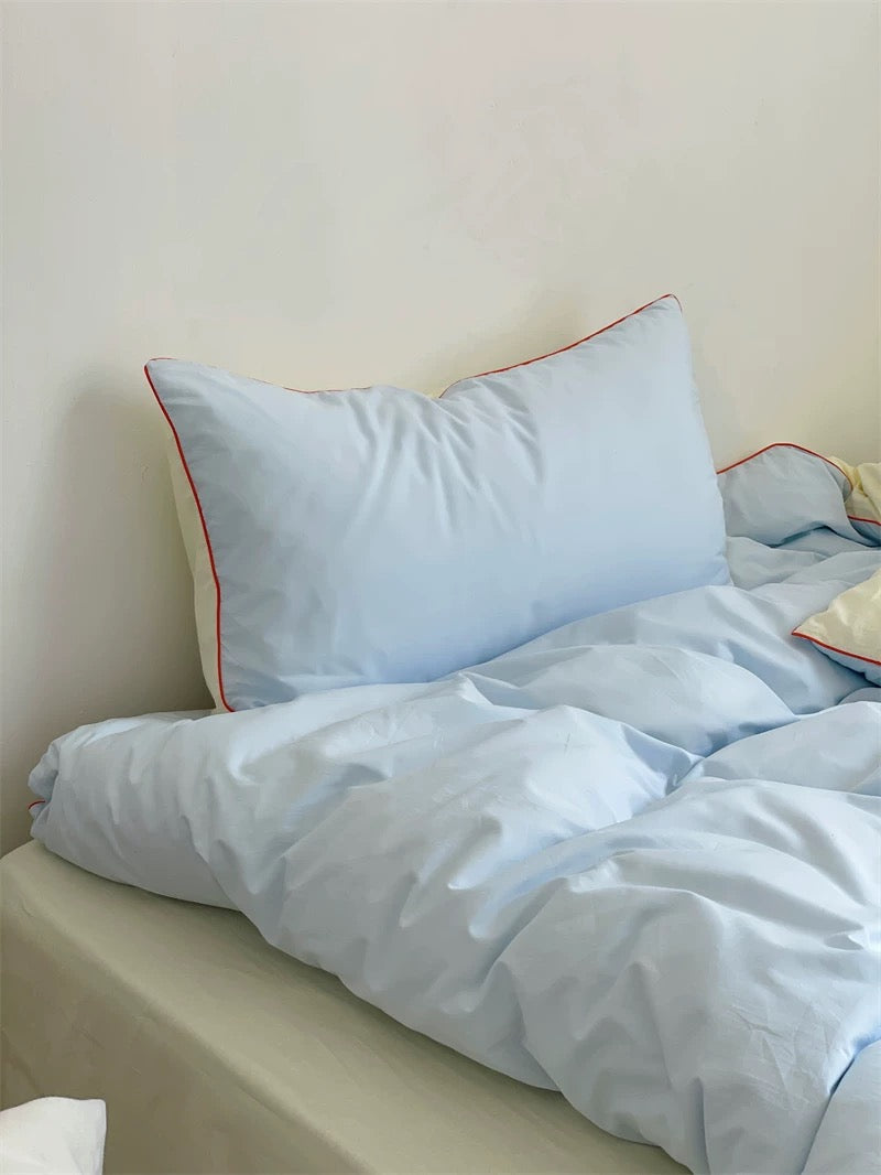 Light blue bedding set with a pillow on a bed against a beige wall.