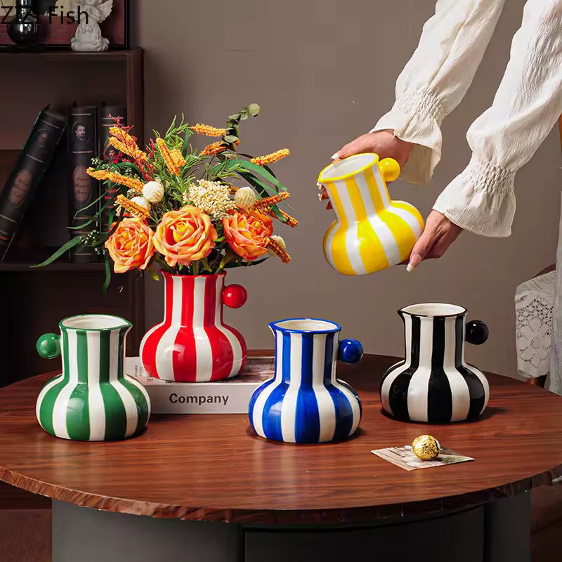 Set of colorful striped vases on a wooden table with a hand holding a yellow and white striped vase.