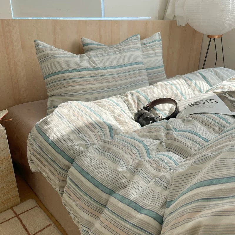 Bed with striped bedding and pillows in a room with a lamp and window.