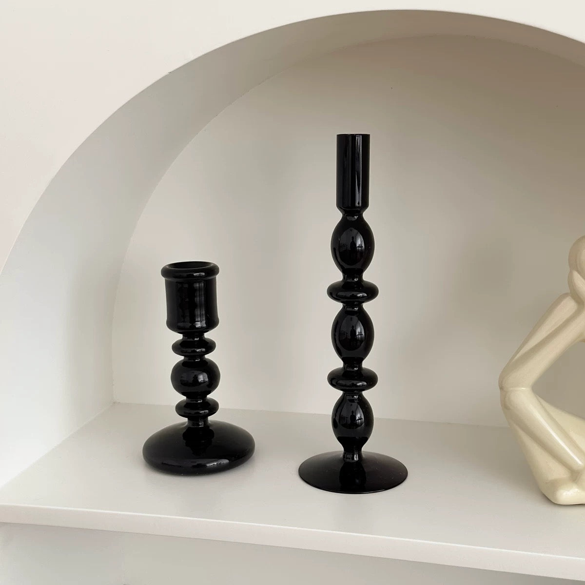 Two black candle holders on a white shelf with a neutral background