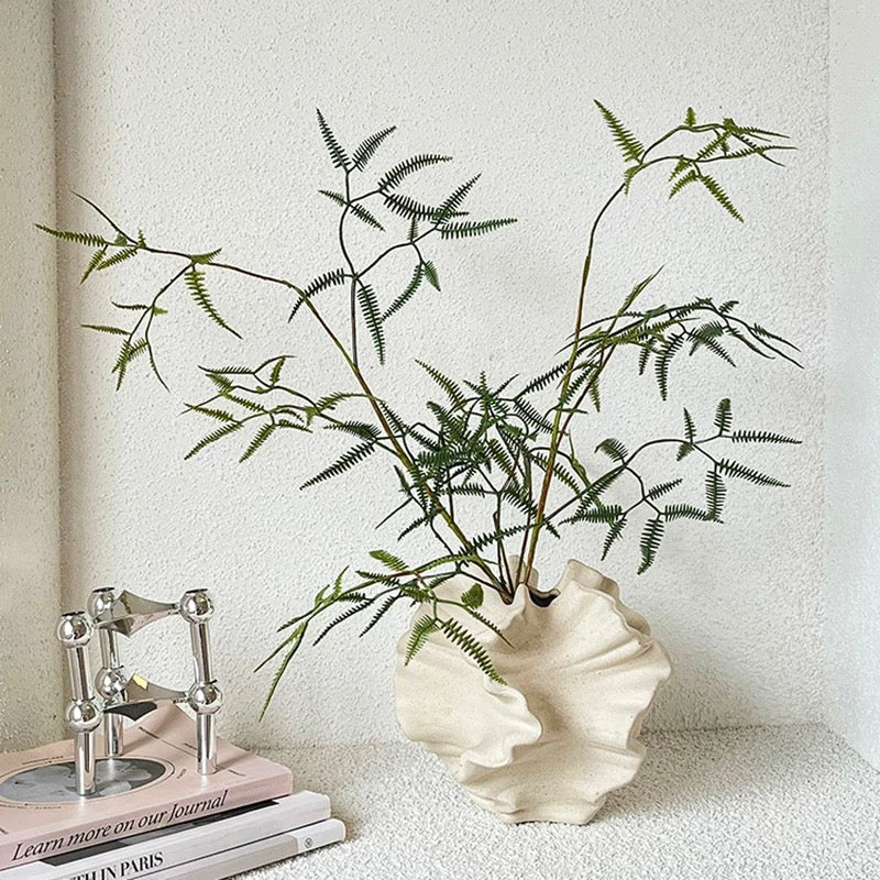 Decorative plant in a shell-shaped vase on a textured surface with a neutral background
