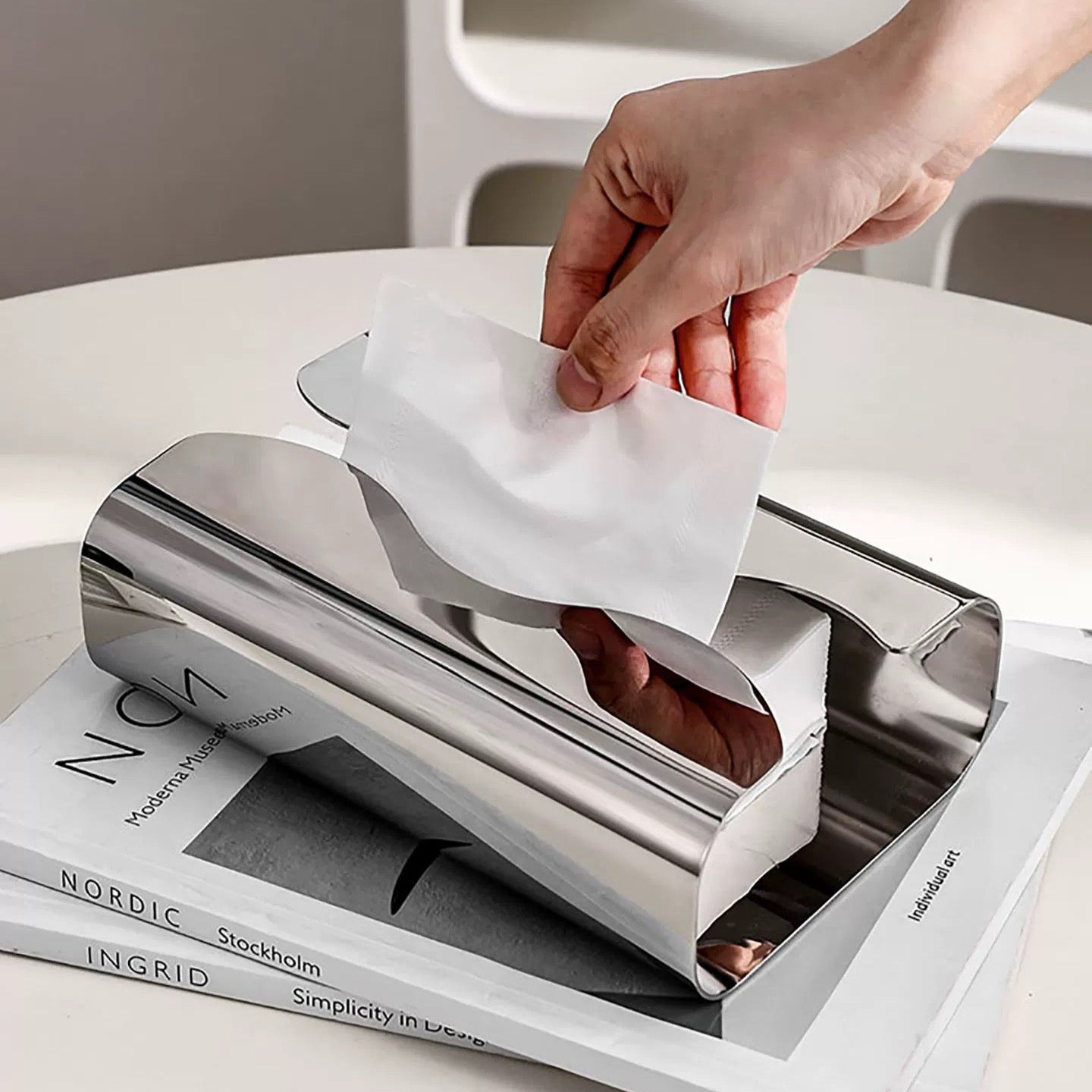 Person using a metallic tissue holder on a stack of books with a minimal background