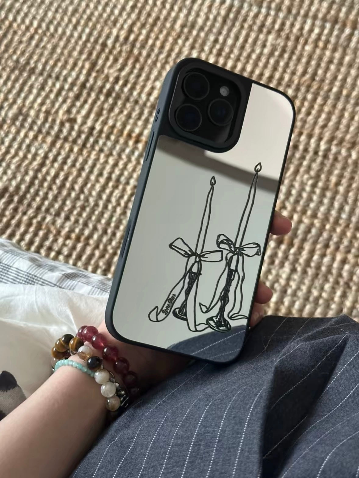 A silver mirror phone case held upright, showing two tall candles tied with bows and black edging.