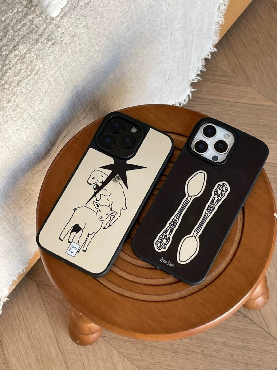 A silver phone case with lamb outlines and a pointed star lies beside the black design with two ornate spoons.
