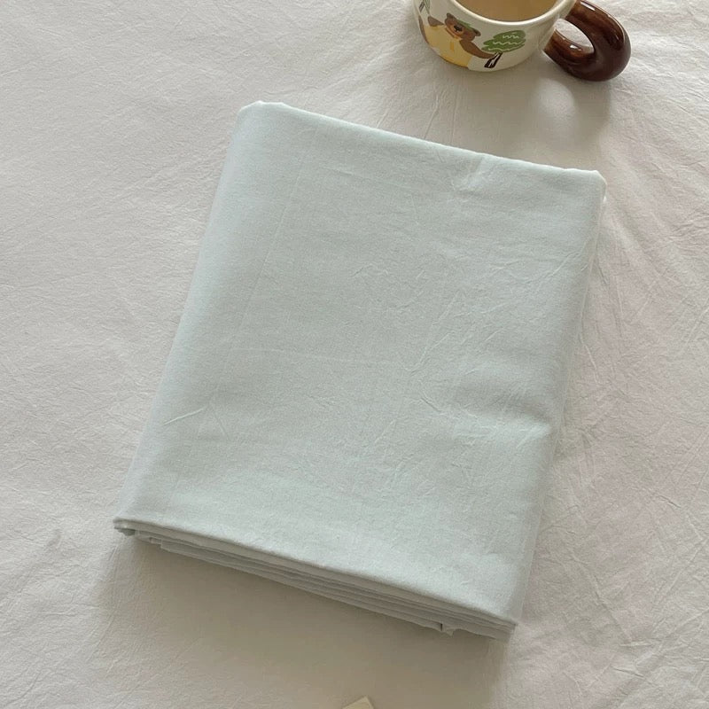 A folded white fabric item, likely a blanket or sheet, placed on a white textured surface with a small decorative mug partially visible in the top right corner.