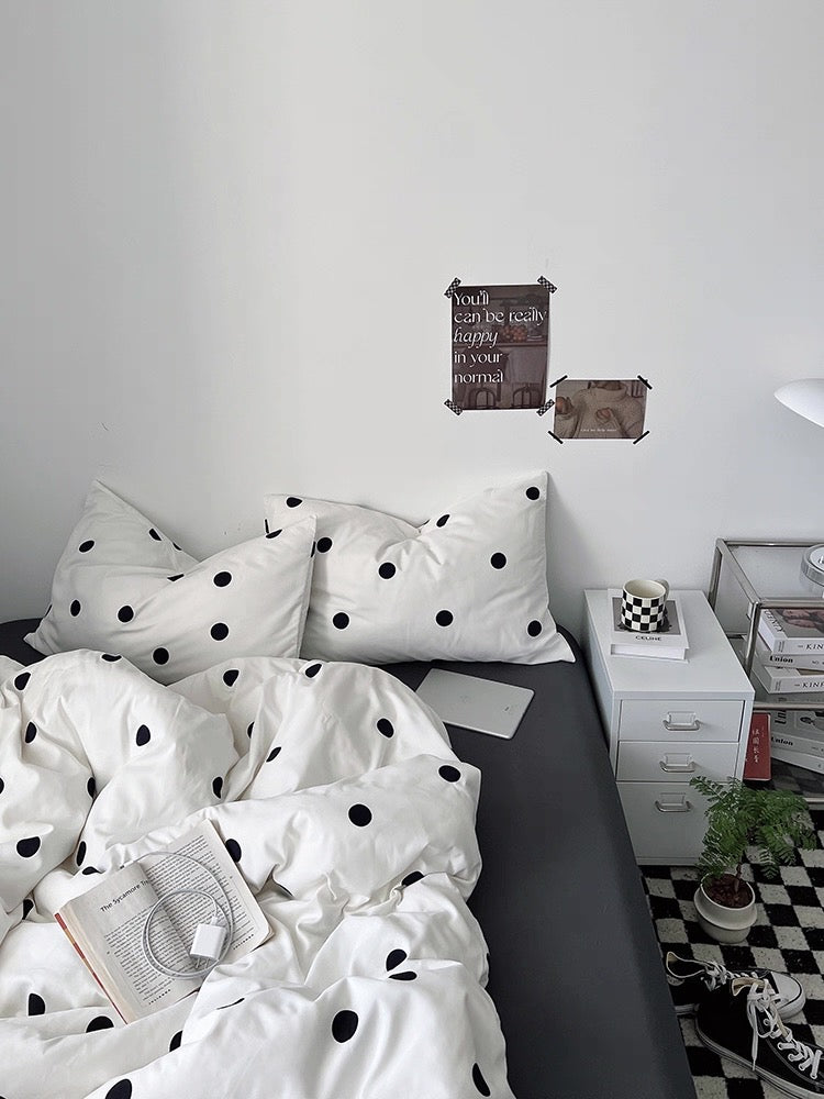 Bed with polka dot bedding in a room with a white wall and checkered floor.