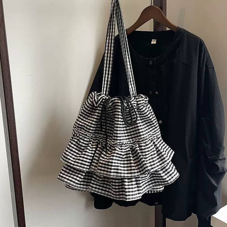 Black and white checkered bag hanging on a hanger with a black shirt in the background.