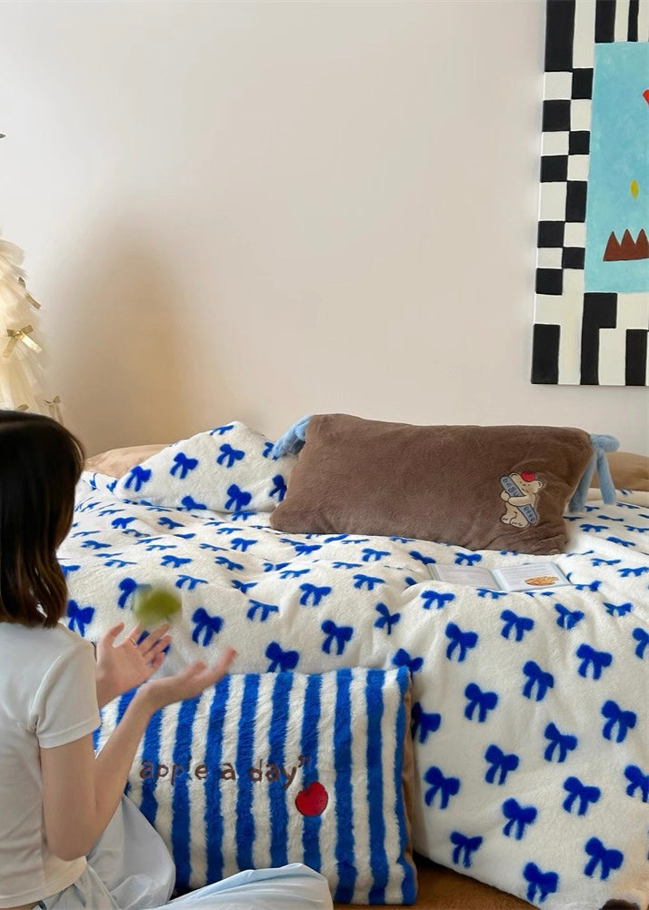 Person sitting on a bed with decorative pillows and a blanket featuring blue patterns.