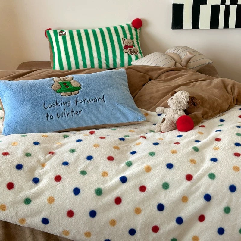 Bed with polka dot blanket, blue pillow with text, and teddy bear.