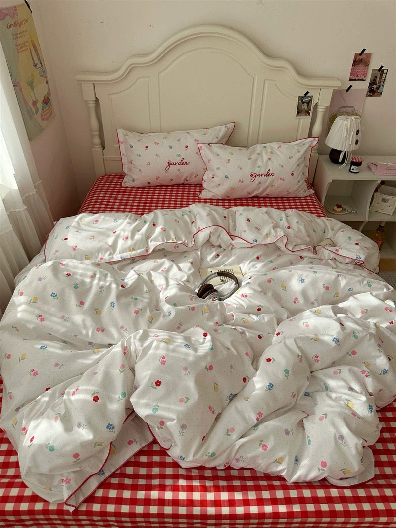 White floral comforter on a bed with red checkered sheets in a bedroom setting.