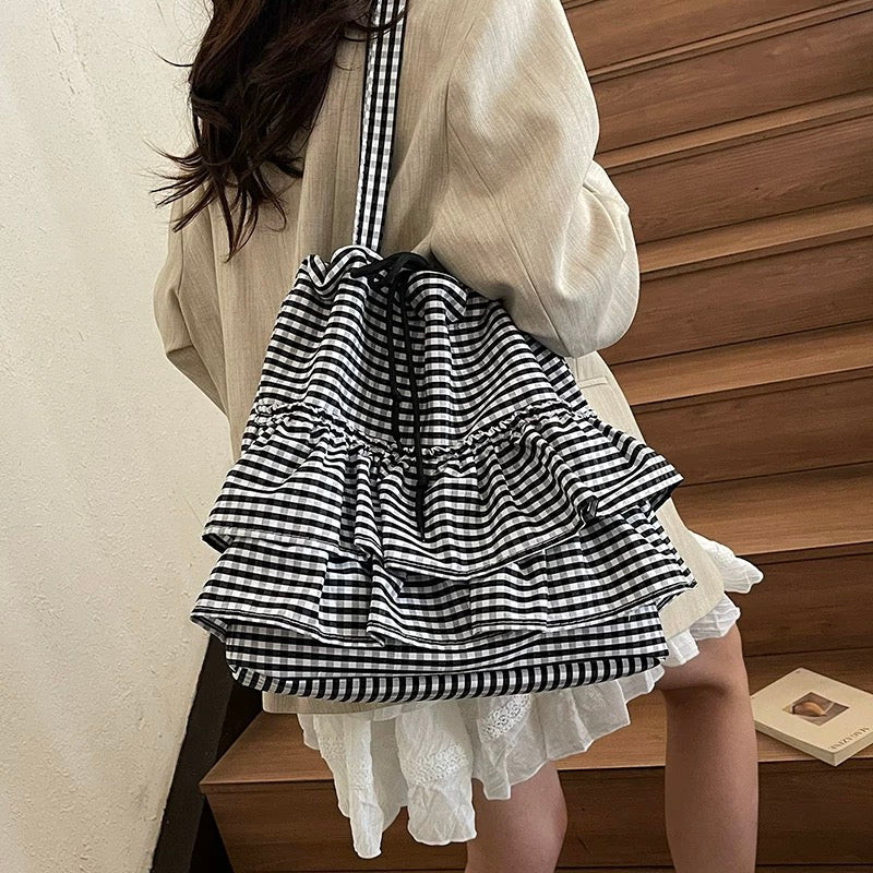 Person wearing a black and white checkered bag with ruffles, standing against a wooden wall.