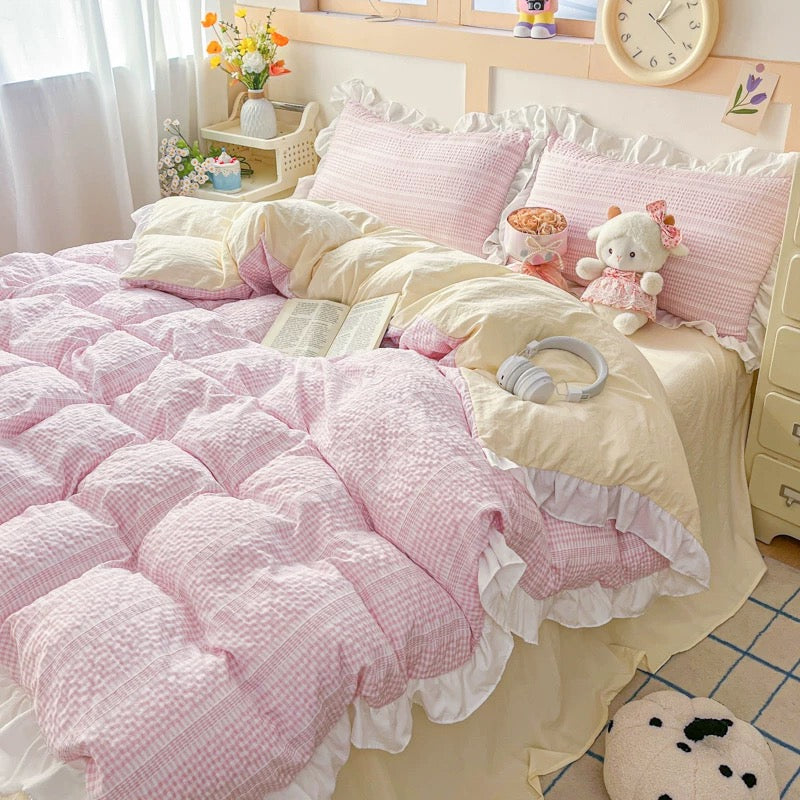 Pink and white bedding set on a bed with decorative pillows and toys.
