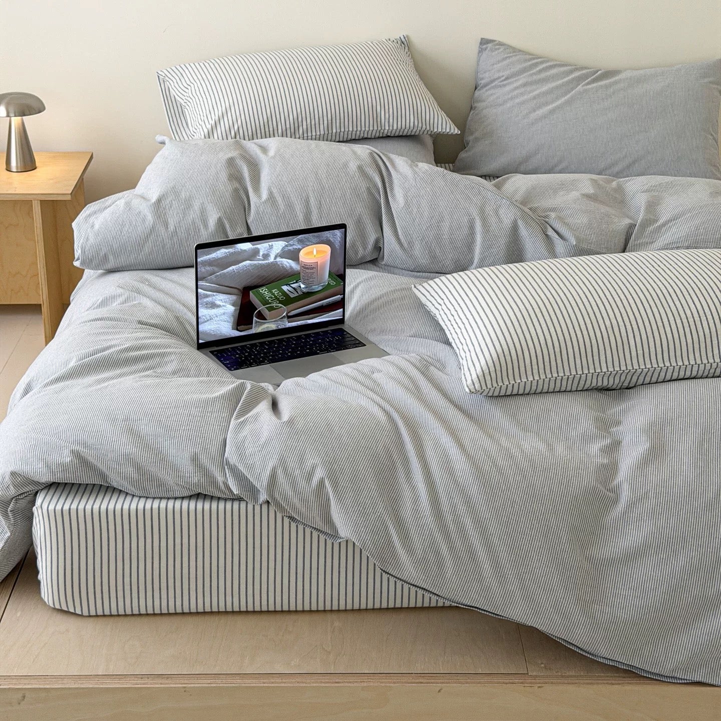 Soft gray cotton bedding featuring delicate pinstripes creating calm Scandinavian sleep space with natural wood furniture indoors.