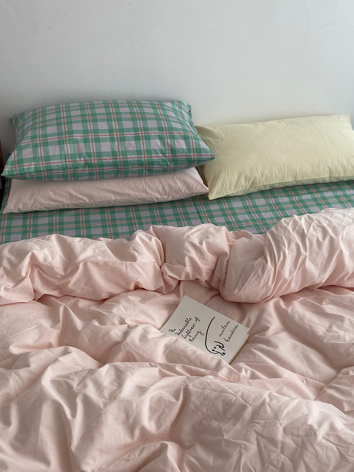 Bed with pink checkered and plain pillows and a pink comforter.