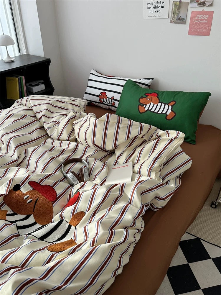 Striped duvet with cartoon dog design on a bed in a room with pillows and a nightstand.