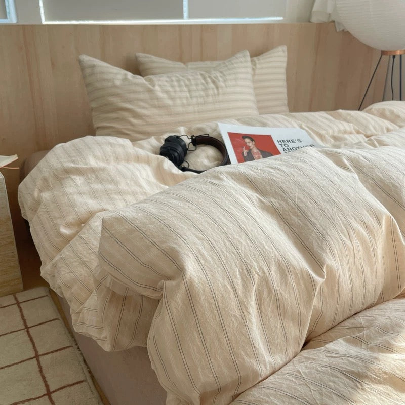 Beige striped bedding on a bed with a magazine and a dog.