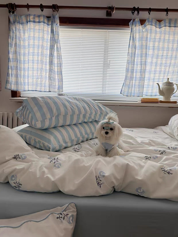 Bedroom with striped pillows and curtains, featuring a small white dog on the bed.