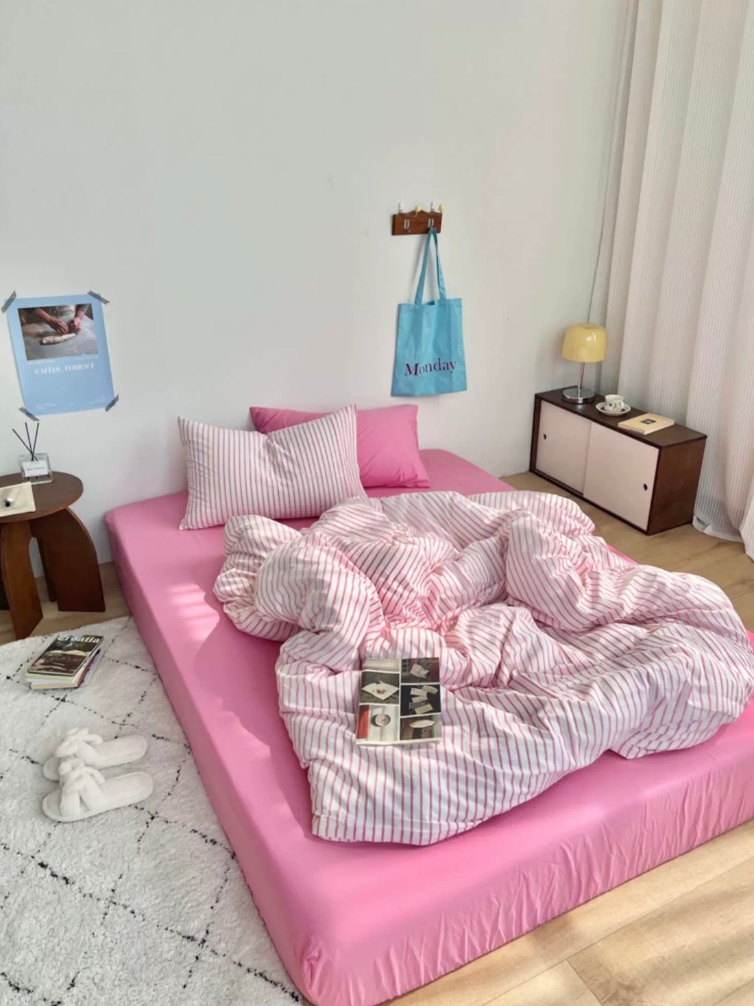 Pink bed with striped bedding in a room with a small table and lamp.