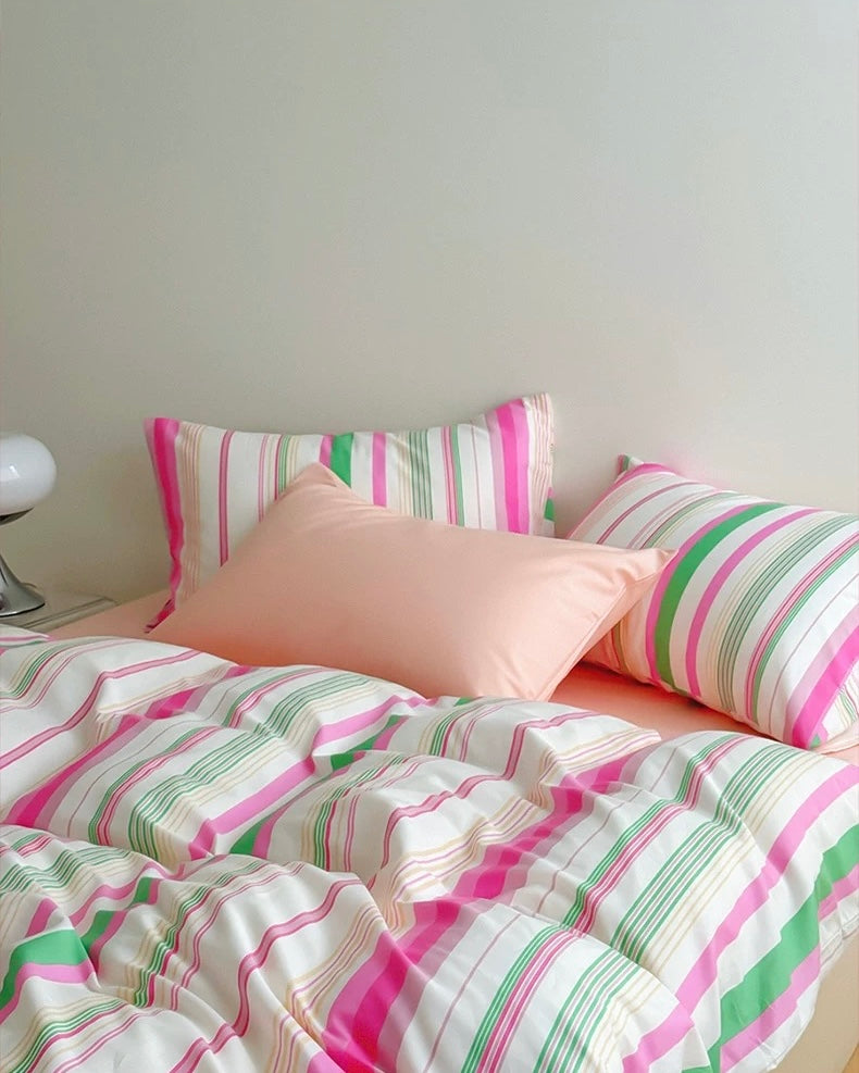 Striped bedding with pink, green, and white pattern on a bed.