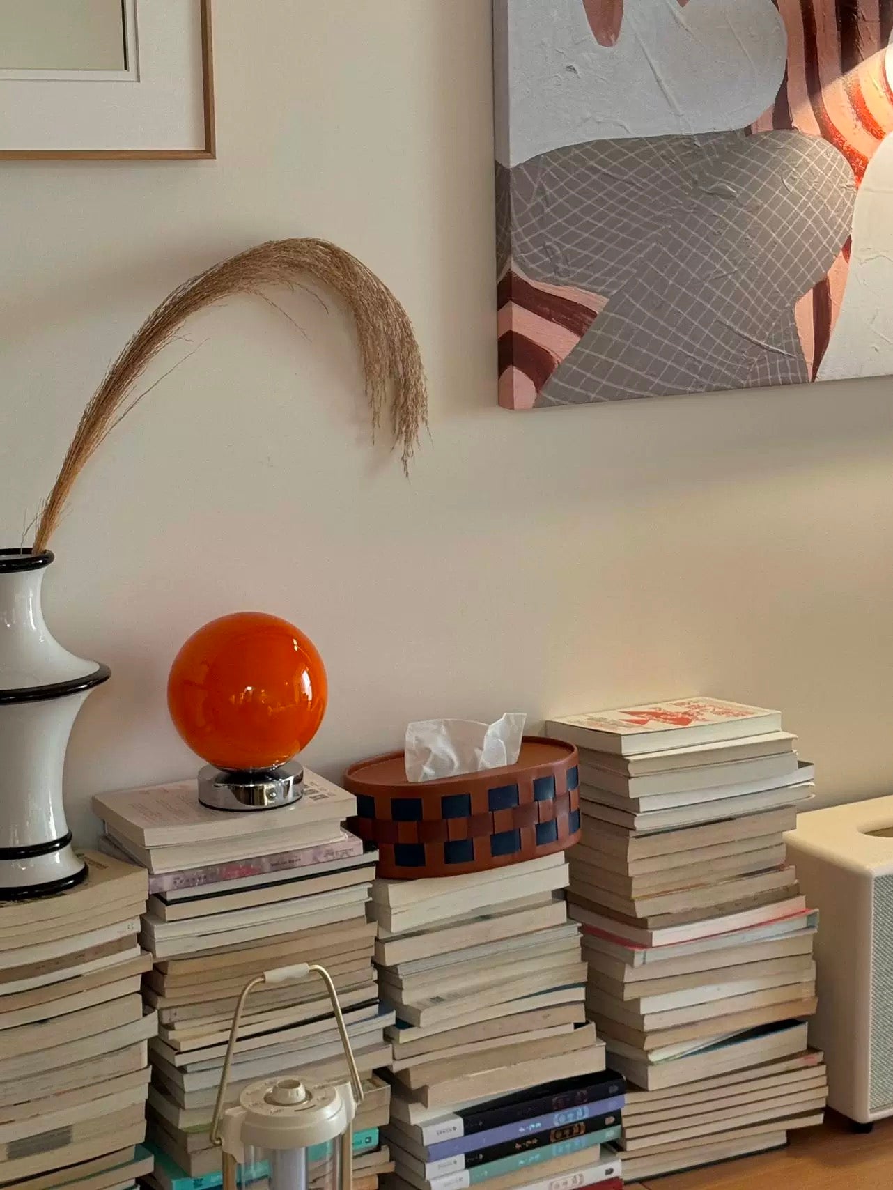 Stacks of books on a surface with decorative items including a vase, orange ball, and basket.