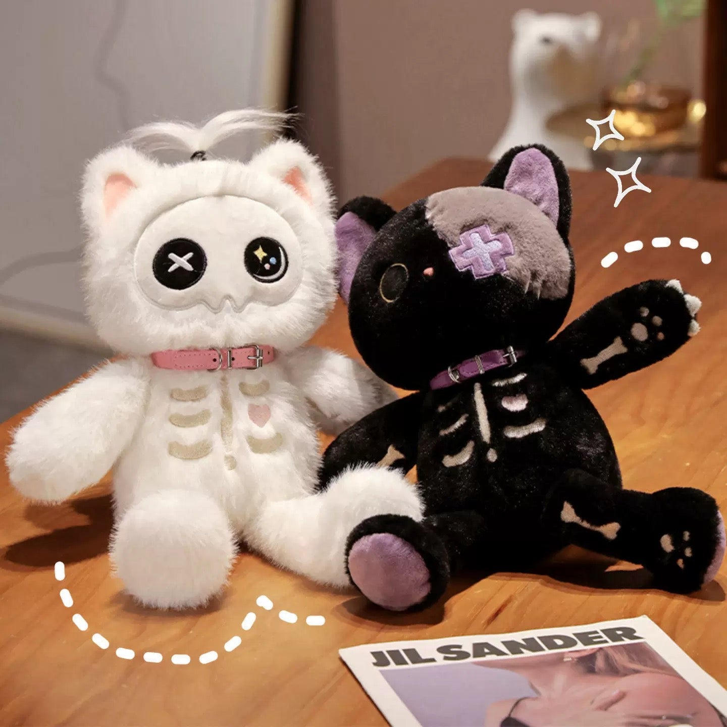 Two skeleton-themed plush toys, one white and one black, on a wooden surface with a Jil Sander magazine.