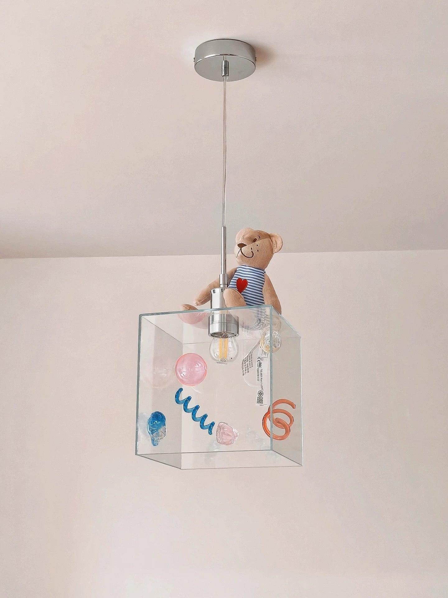 Children's pendant light with a clear glass shade featuring colorful designs and a teddy bear toy inside.