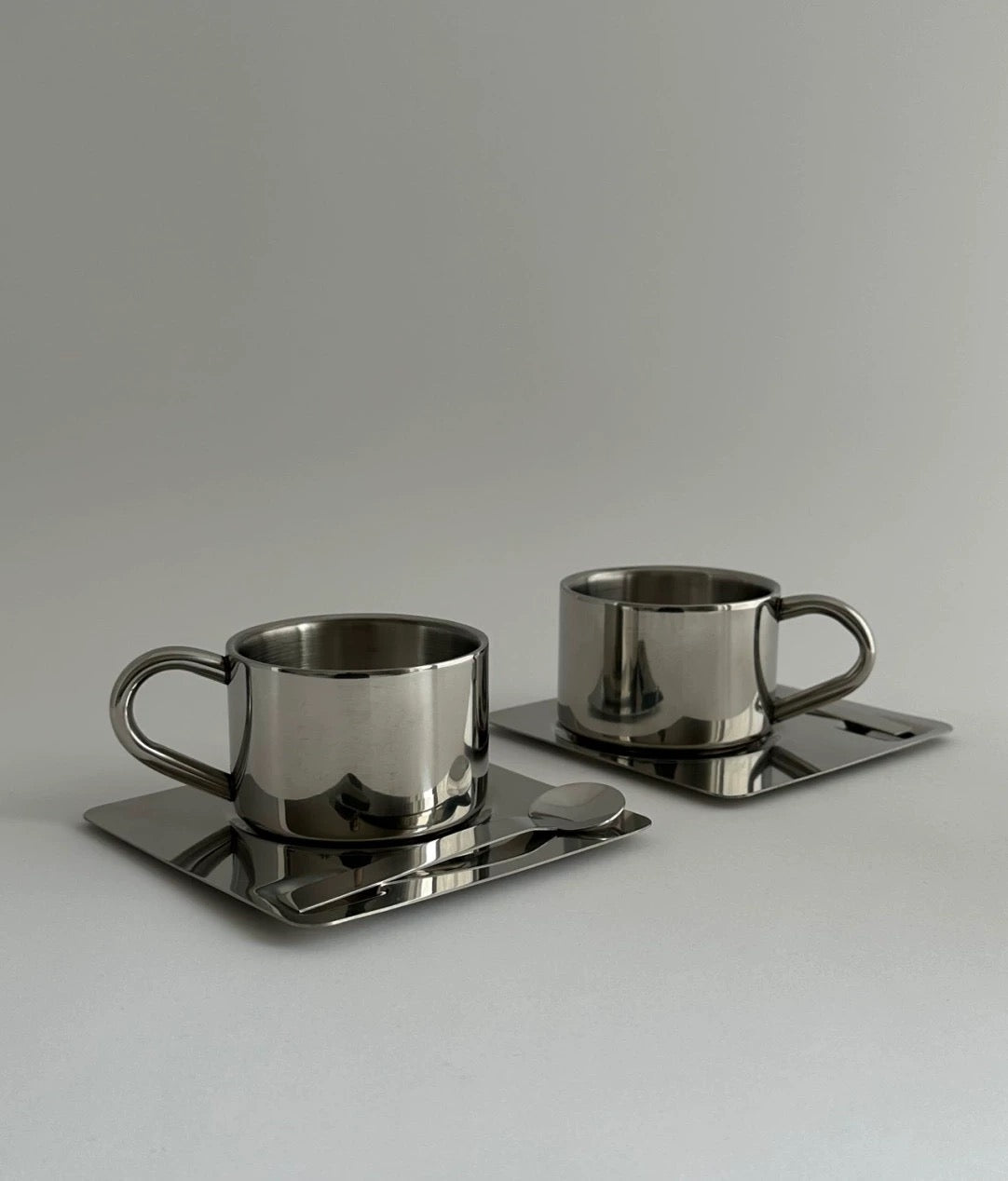 Two metallic cups with saucers on a reflective surface