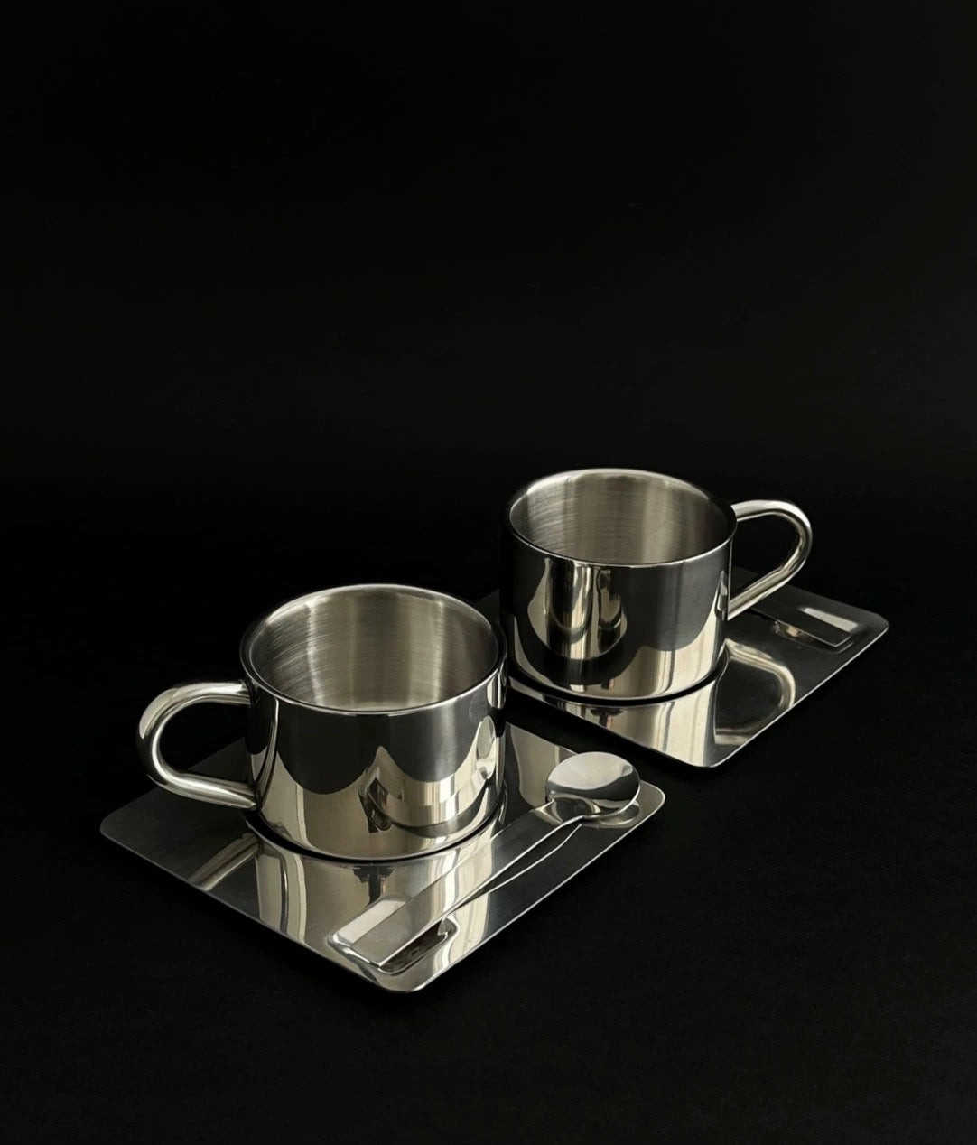 Two metal cups on a matching tray against a black background