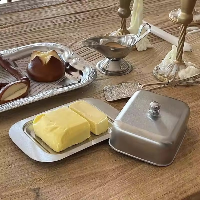 Butter dish with two sticks of butter on a wooden table with silver lid and tray.
